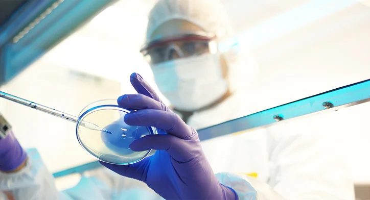 Scientist in protective equipment handling a petri dish in a containment lab